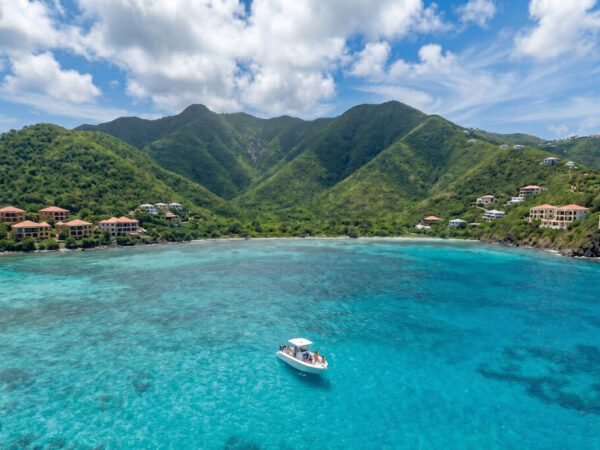Wide aerial view of a group of passengers on a speedboat tour in the turquoise waters of St. Maarten with tropical mountains and villas.