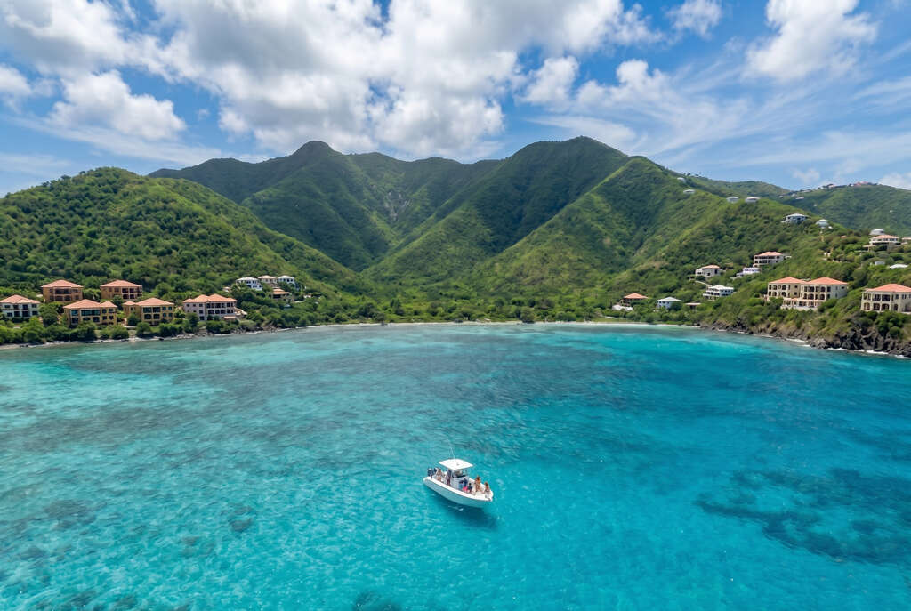 Wide aerial view of a group of passengers on a speedboat tour in the turquoise waters of St. Maarten with tropical mountains and villas.
